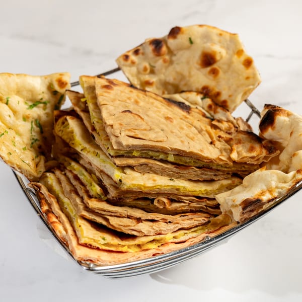 A metal basket filled with various Nepalese flatbreads, including plain naan and stuffed paratha.