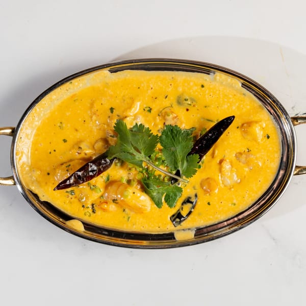 Nepalese shrimp curry in a silver oval dish, garnished with cilantro and dried red chilies.