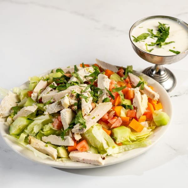 Chicken salad with lettuce, tomatoes, cucumbers, and cilantro, served with a side of creamy dressing.