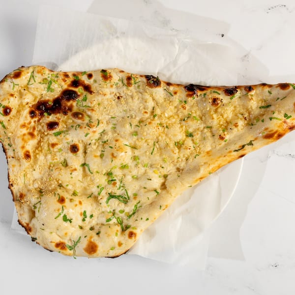 Golden-brown garlic naan bread, topped with chopped green herbs, on white parchment paper.
