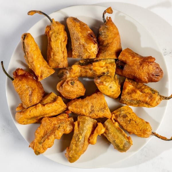 A white plate filled with golden-brown, battered chili peppers, a Nepalese delicacy.