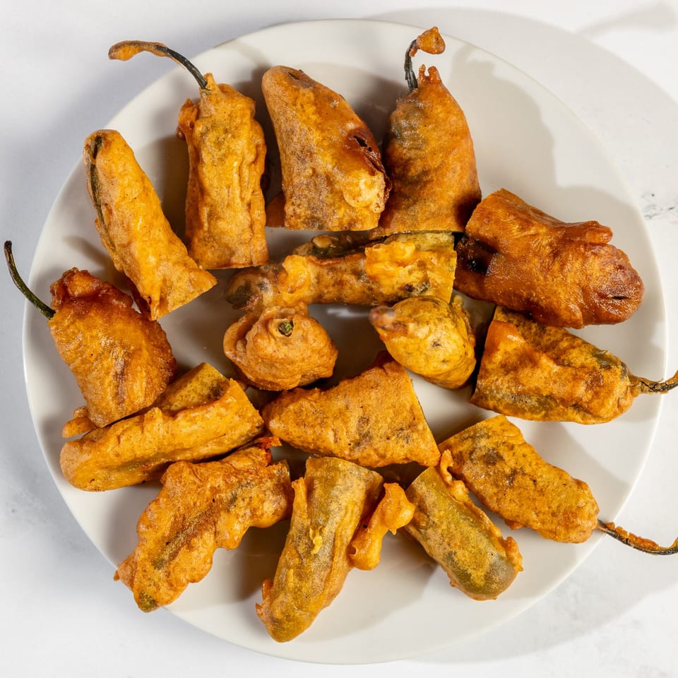 A white plate filled with golden-brown, battered chili peppers, a Nepalese delicacy.
