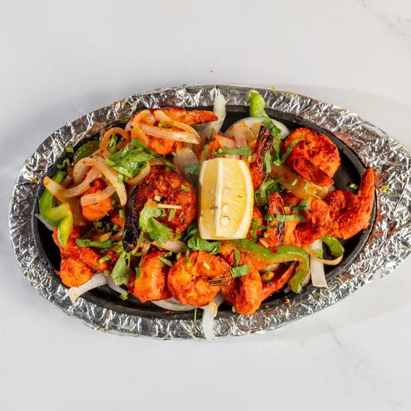 Sizzling shrimp with onions, green peppers, and cilantro, garnished with a lemon wedge.