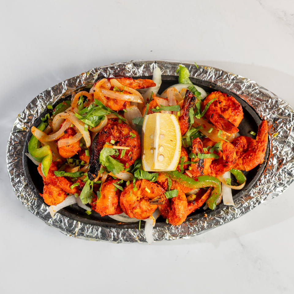 Sizzling shrimp with onions, green peppers, and cilantro, garnished with a lemon wedge.