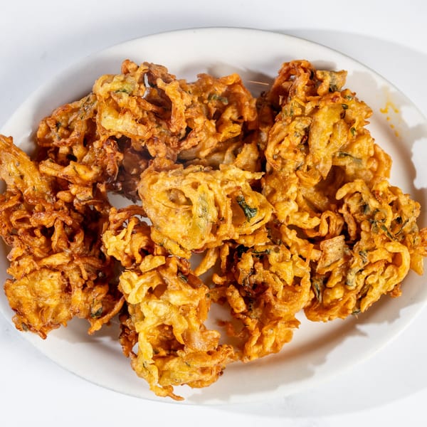 A white plate filled with golden-brown, crispy Nepalese vegetable pakoras, showcasing their textured surface.