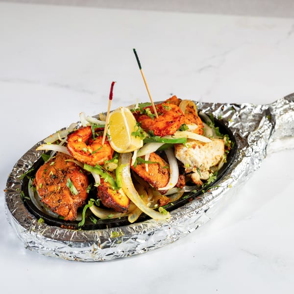 Sizzling platter of Nepalese chicken and shrimp tikka with onions, peppers, and a lemon wedge.
