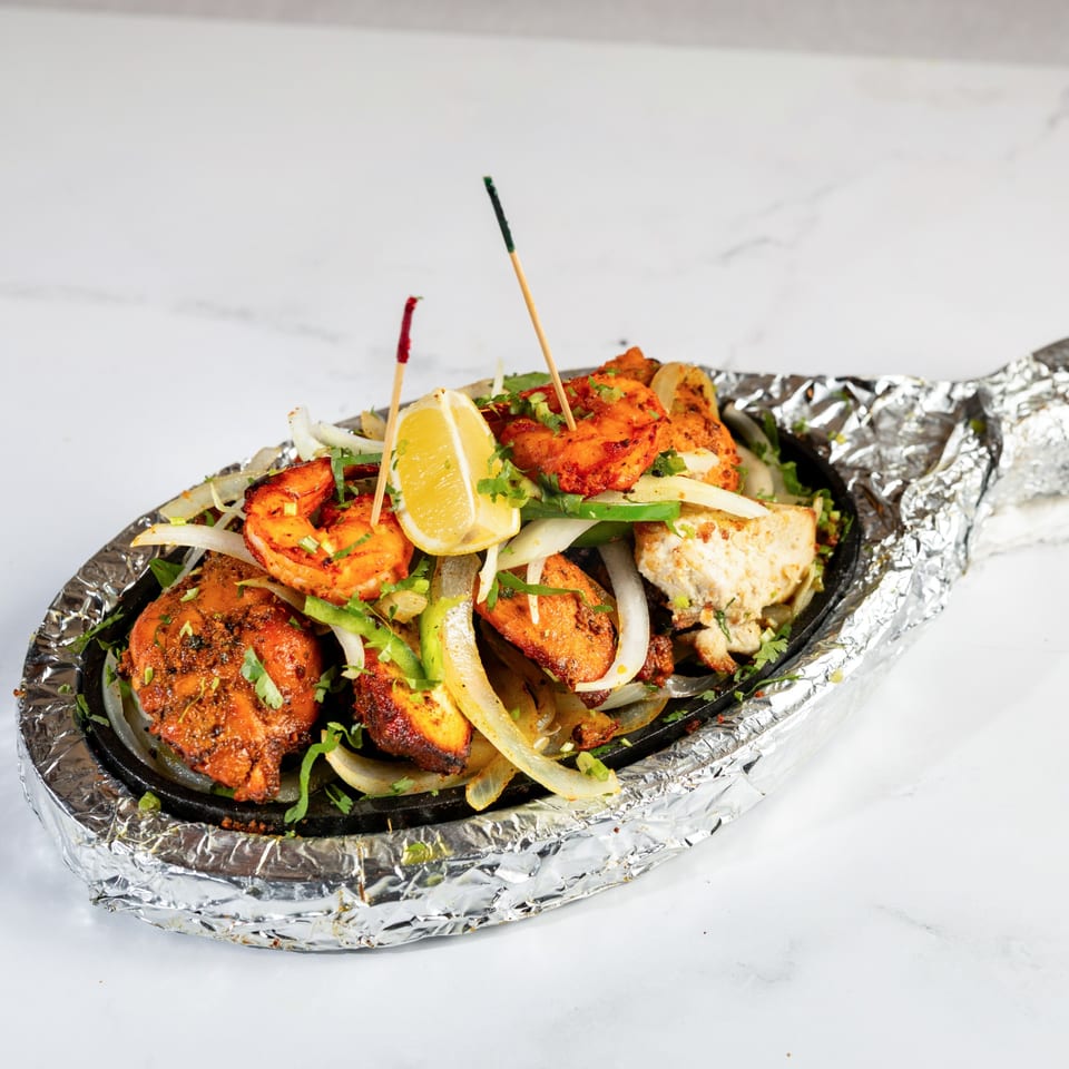 Sizzling platter of Nepalese chicken and shrimp tikka with onions, peppers, and a lemon wedge.